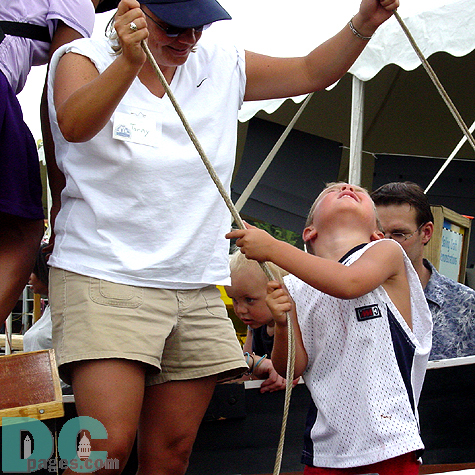 This little boy is on the road to being a tip-top sailor someday.  He watches as his action of pulling the main sail's rope causes it to rise up to catch the wind.