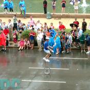 A juggler on a unicycle performs down the street.