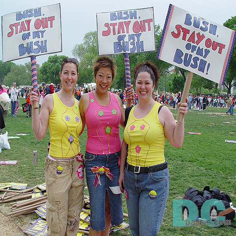 Three Pro-Choice activists hold up their demonstration signs - BUSH, STAY OUT, OF MY BUSH. The three women designed shirts with a picture outline of a female body with flowers covering the reproductive organs.