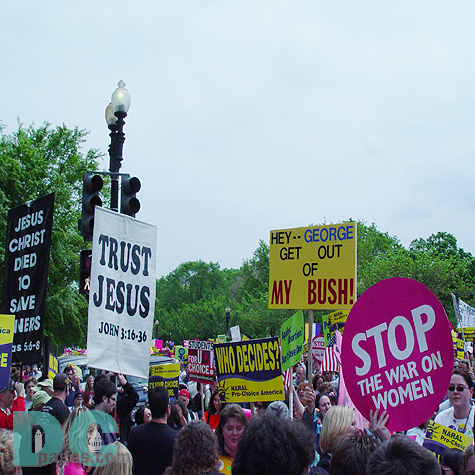 Marchers on Constitution Avenue.  One marcher holds a message for the President - HEY -- GEORGE GET OUT OF MY BUSH while another holds a pink sign reading STOP THE WAR ON WOMEN.