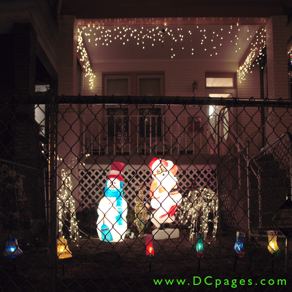 A bright snowman and Santa are accompanied by two white reindeer and a string of white lights.