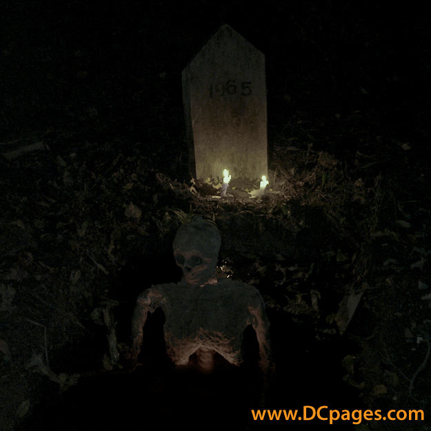 This skeleton hangs by its neck underneath its tombstone.