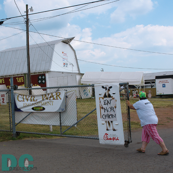 Parking lot view of the entrance gates to the Prince William County Fair. Sign left - CIVAL WAR ENCAMPMENT. Sign right - Advertisement - EAT MORE CHICKEN