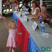 A blond haired baby girl in a pink Washington Redskins dress walks past the judges. 