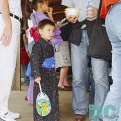 Among tall adults, a little boy was standing with a hand fan next to his sister. 