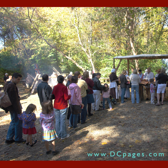 A line of adults and children eagerly wait for some tasty colonial food. 