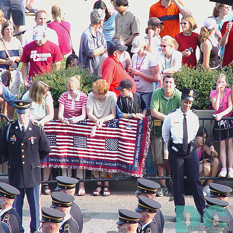 A family drapes a quilt over the baricades with the script "Indivisible, with Liberty and Justice for All".