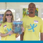 ICAF staff Amanda Kah and Chris Miles hold the festival issue of the ChildArt Magazine in front of the Child Finalist Art display