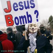 A demonstrator dressed in a Guy Fawkes mask (based on anarchist comic character named "V"), holds up a sign that states - Would Jesus Bomb? 