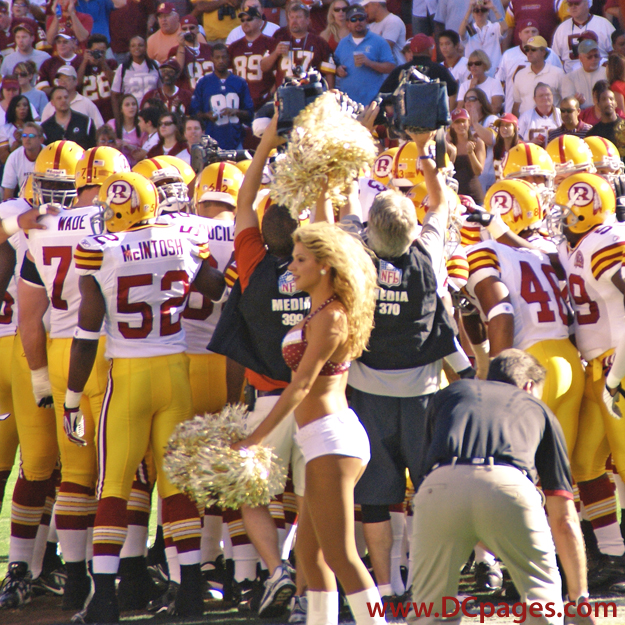 The Redskin team huddles together before the start of the game. The team is wearing vintage jerseys celebrating their 75th anniversary. There is an R instead of the current indian head. The uniform is a bright yellow and with barbeque red numbers and stripes.
